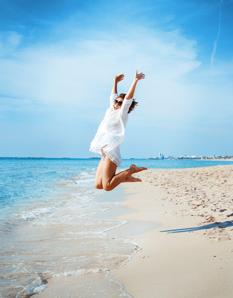 Young woman in cover up jump on the beach