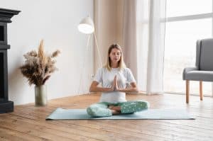 Caucasian young nice-looking pregnant woman sitting on fitness mat in lotus position meditating
