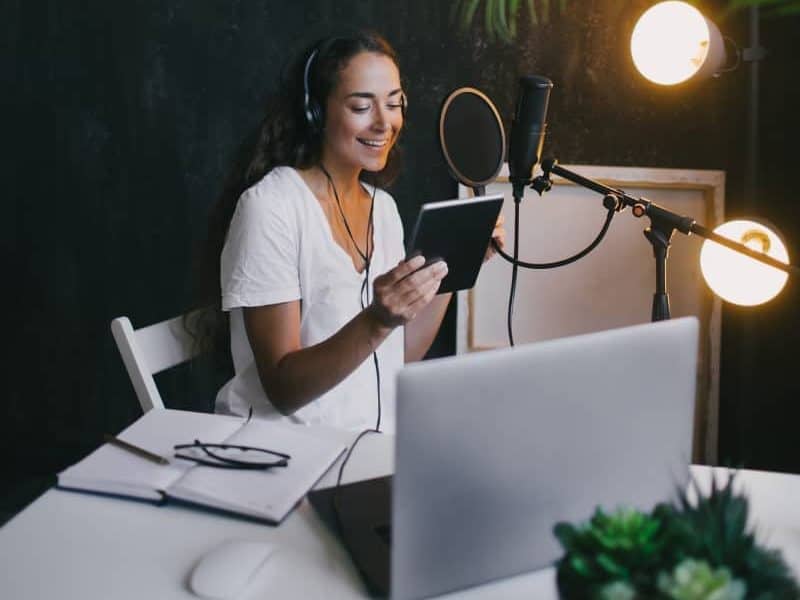 Young woman blogger recording podcast using microphone, tablet and laptop in a studio.